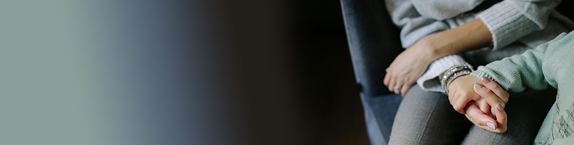 A mother and child sit close together, one person gently holding the other’s hand in a comforting gesture.