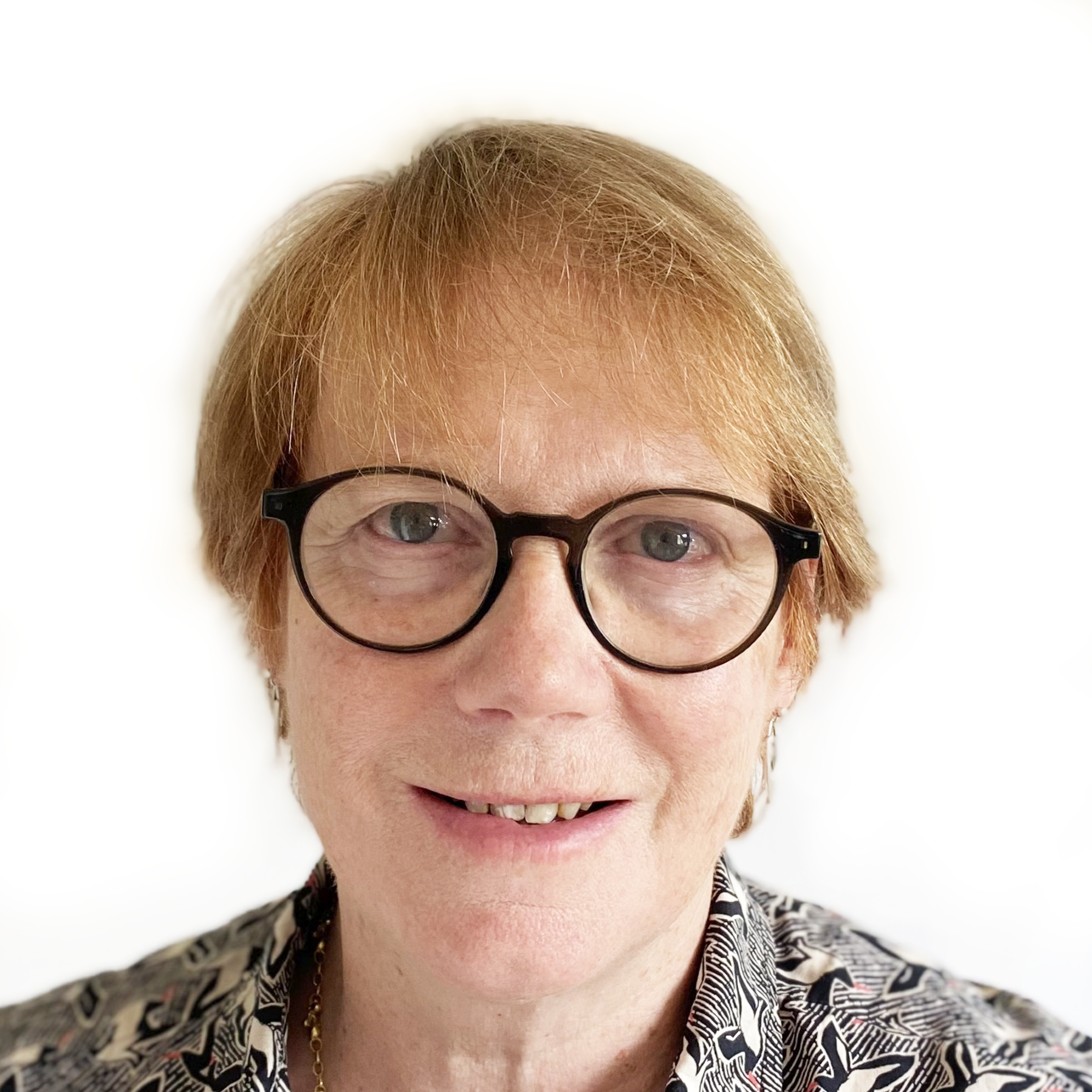 Smiling person with short light hair and glasses wearing a patterned shirt against a white background.