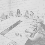 Eight women write and smile while seated around tables in a meeting room, with handwritten notes visible as an overlay on the image.
