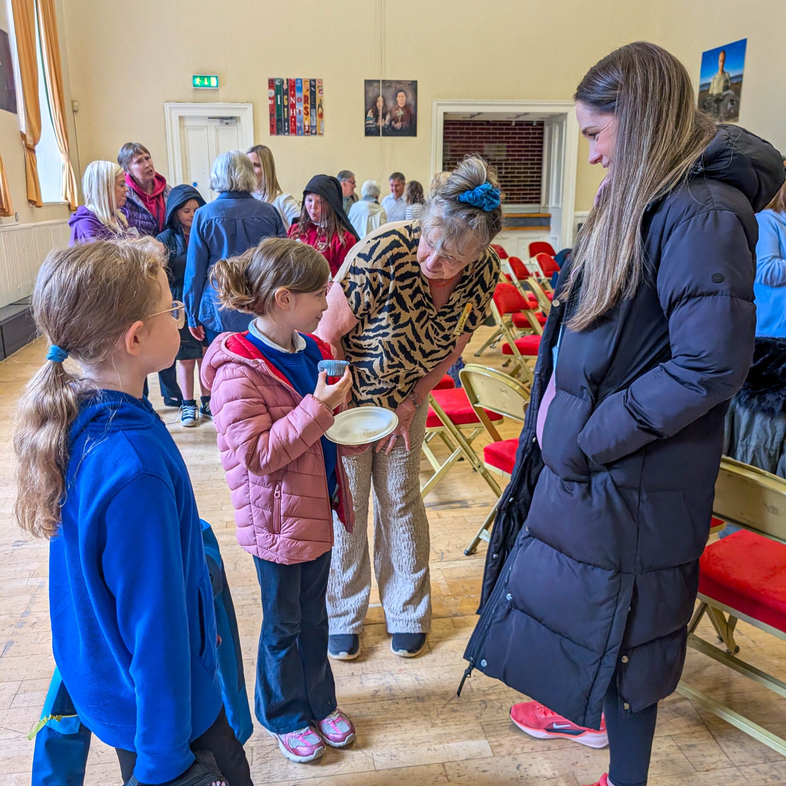 People chatting and smiling in a room with red chairs, with two girls standing next to two women.